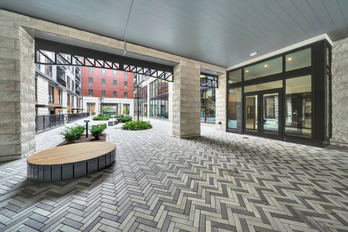 Covered courtyard with herringbone brick, stone pillars, wood bench, and building views.