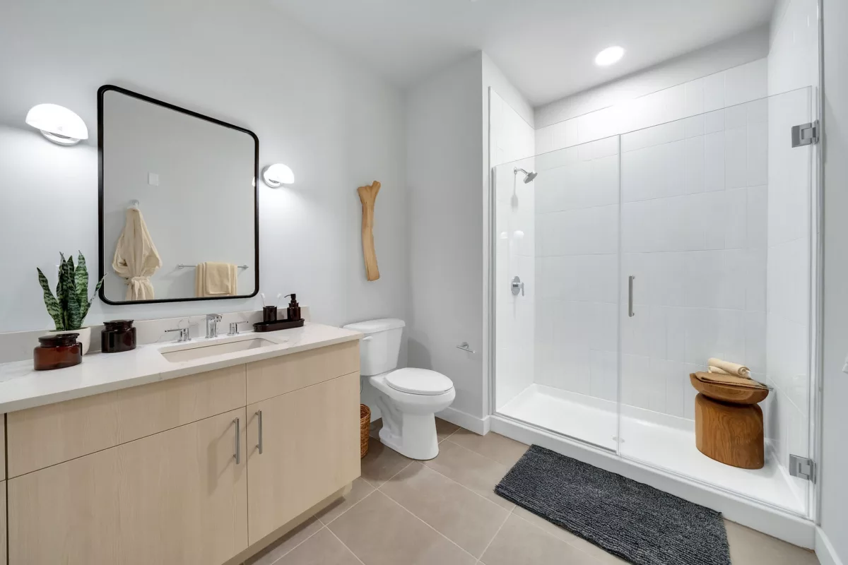 Bathroom with wood vanity, quartz countertop, glass shower, and gray tile floor.