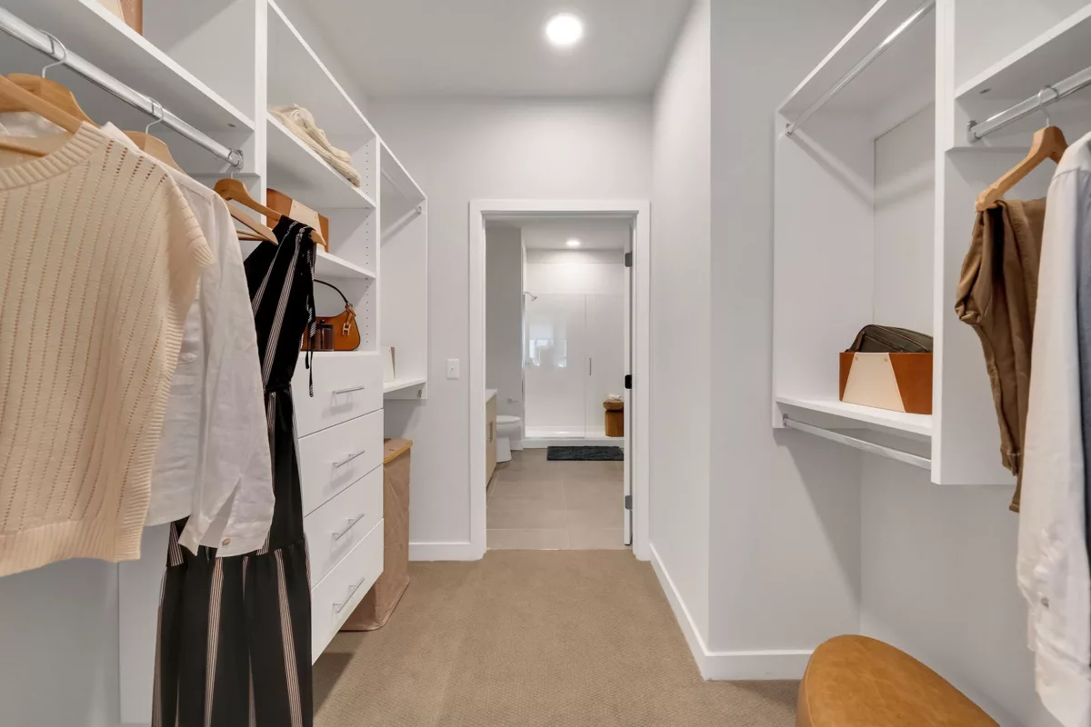 Oversized closet with white shelving and hanging clothes, leading to a bathroom with glass shower.