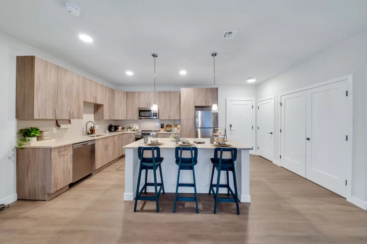 Kitchen with wood cabinets, island with seating, stainless steel appliances, and wood floors.