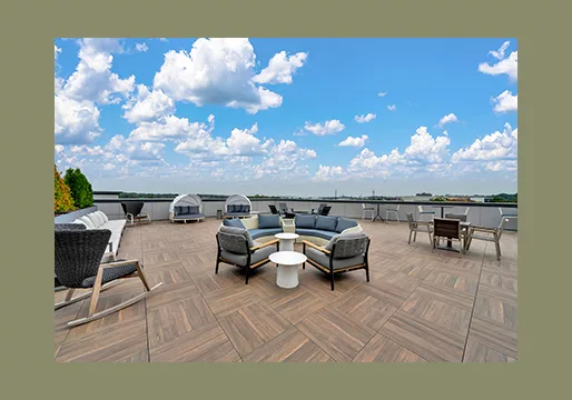 A photo of a rooftop deck with tables and chairs under a blue sky, on a green background.