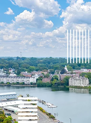 An aerial photo of a river with apartment buildings and trees in the background under a blue sky with white clouds.