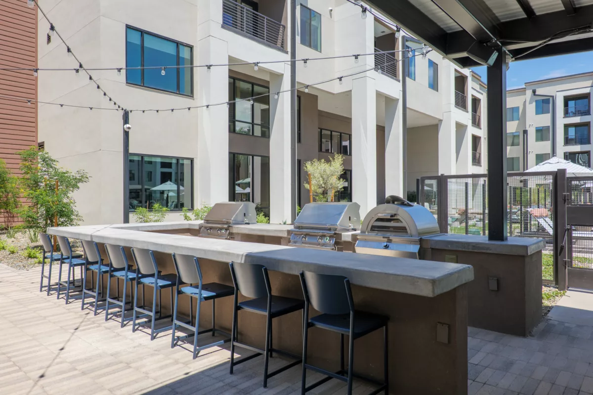 Outdoor grilling area with stainless steel grills, concrete bar, and barstool seating.