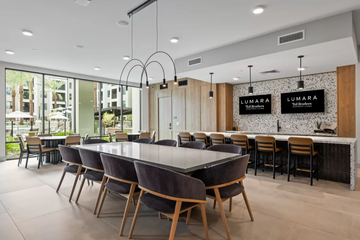 Community room with large table, chairs, bar seating, and outdoor views.
