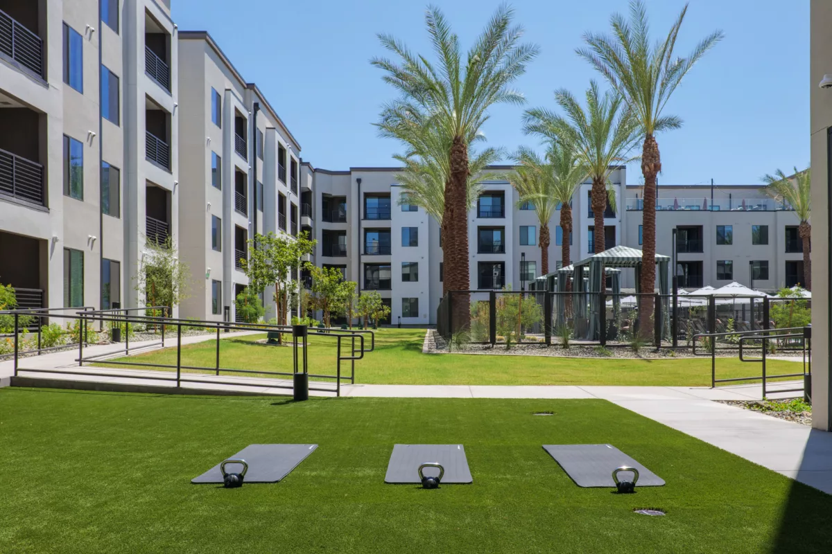 Outdoor fitness area with mats and kettlebells on artificial turf, buildings and palm trees in...