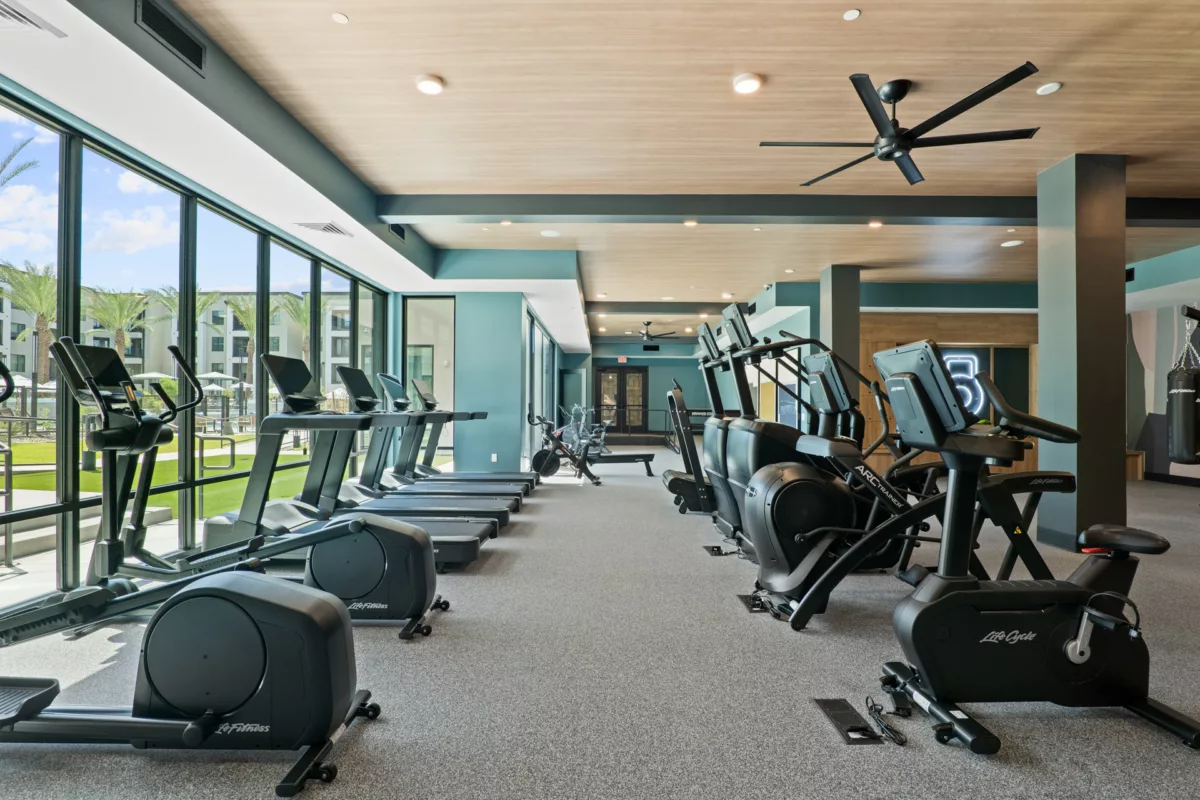 Fitness center with treadmills, ellipticals, bikes, and rowing machines on gray carpet.