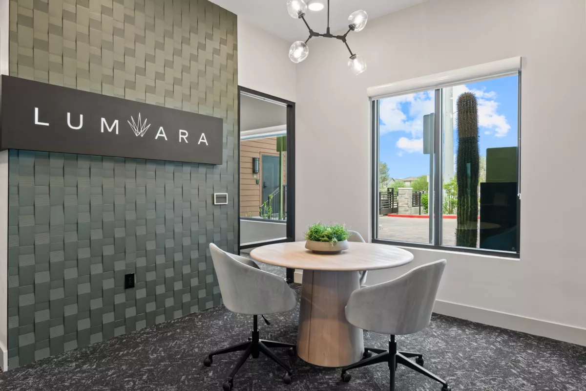 Modern meeting area with round table, chairs, and view of exterior landscaping. Textured wall.
