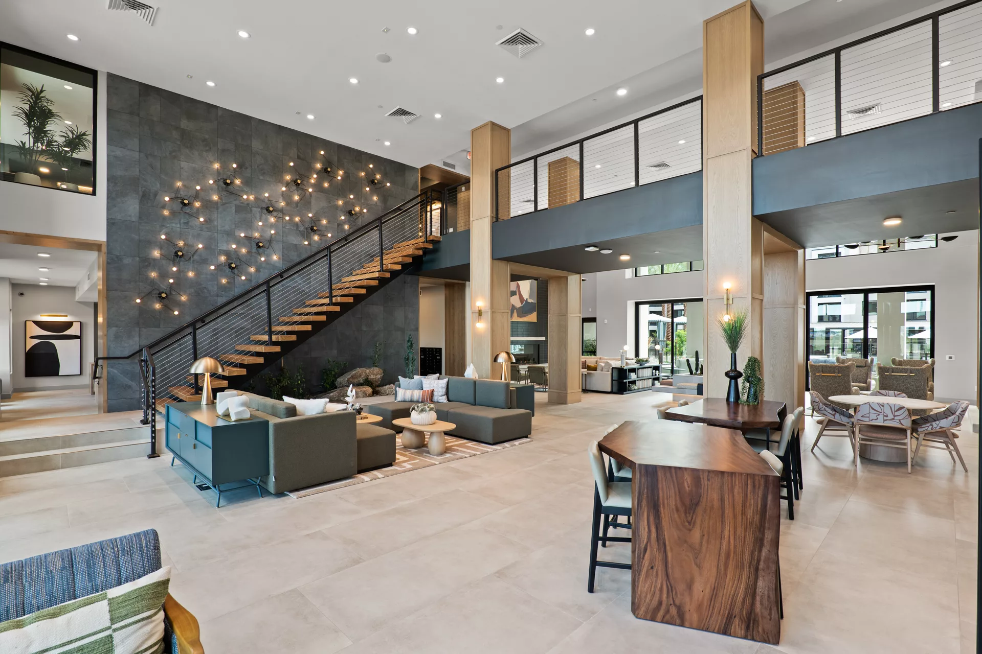 Modern lobby with seating, wood tables, and staircase with decorative wall lighting.