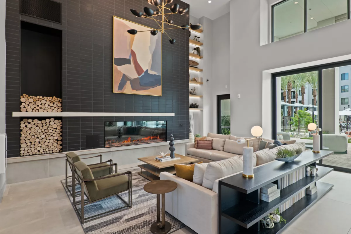 Modern lounge with fireplace, sofas, and view to outdoor area with palm trees.
