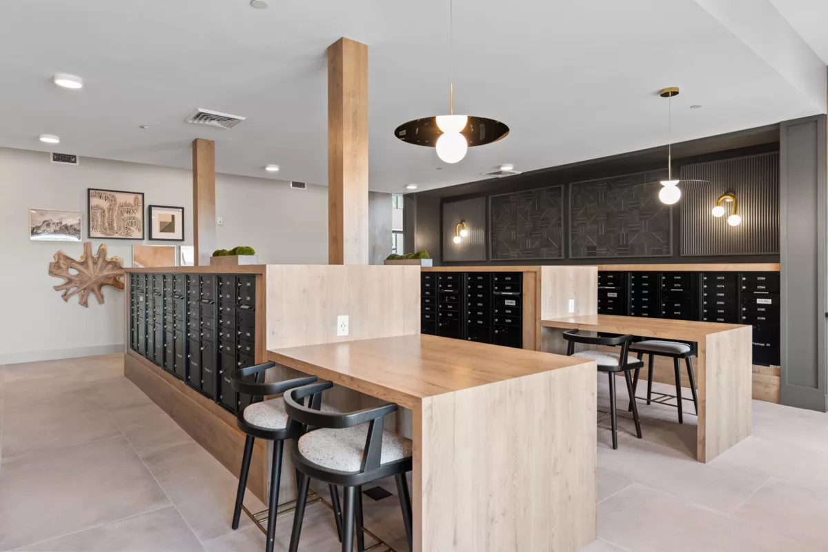 Mailroom with black mailboxes, wood desks, and chairs under modern pendant lighting.