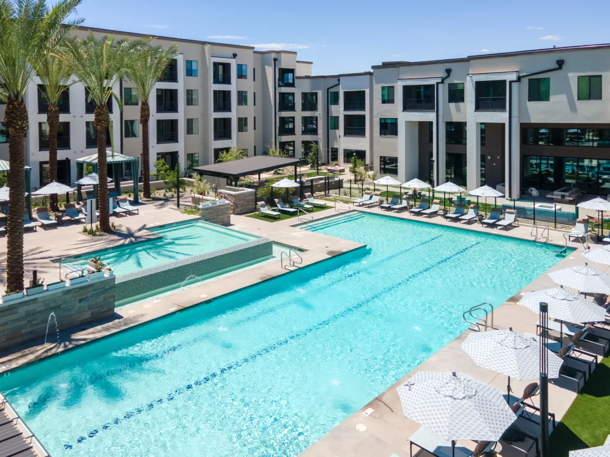 Aerial view of a large pool with lounge chairs and umbrellas surrounded by apartment buildings.
