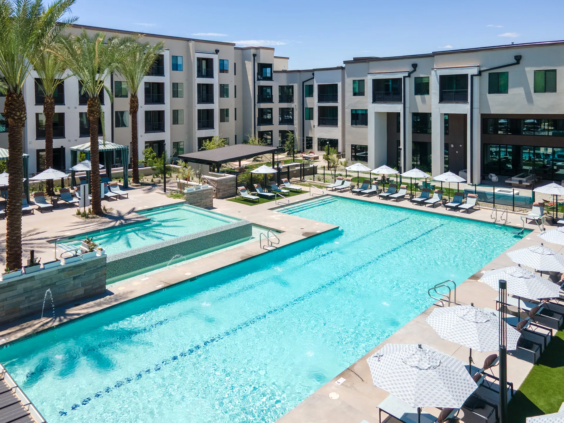 Aerial view of a large pool with lounge chairs and umbrellas surrounded by apartment buildings.