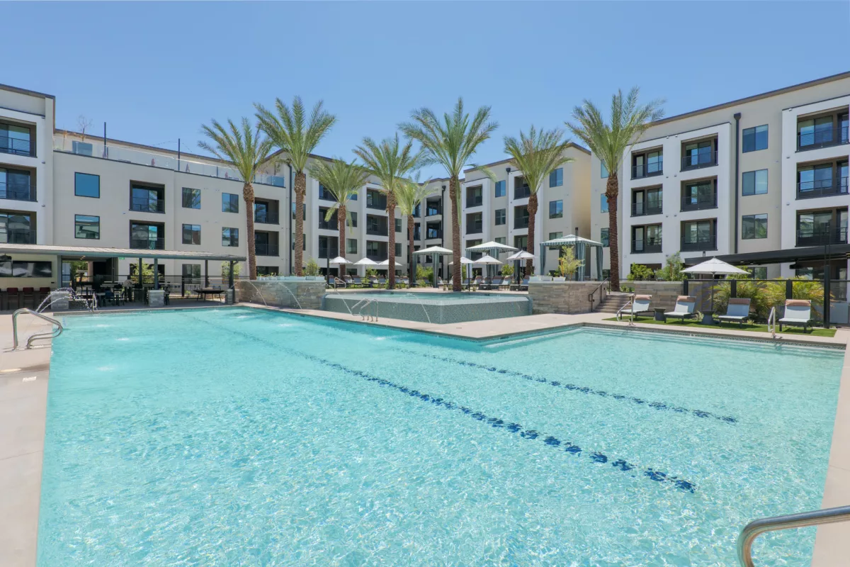 Outdoor pool with lounge chairs, palm trees, and multi-story building in the background.