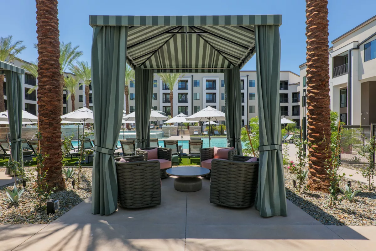 Cabana with striped awning and curtains overlooks pool with lounge chairs and apartment buildings.