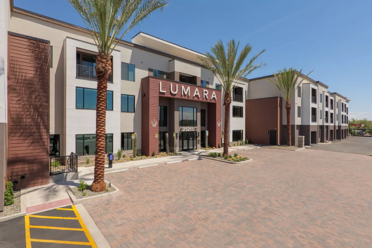 Exterior view of a modern apartment building with palm trees and brick paved parking area.