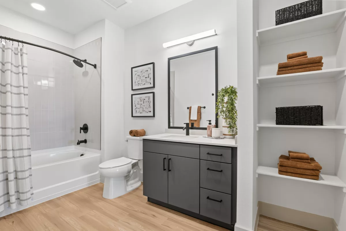 Bathroom with gray vanity, white quartz countertop, and open shelving with towels.