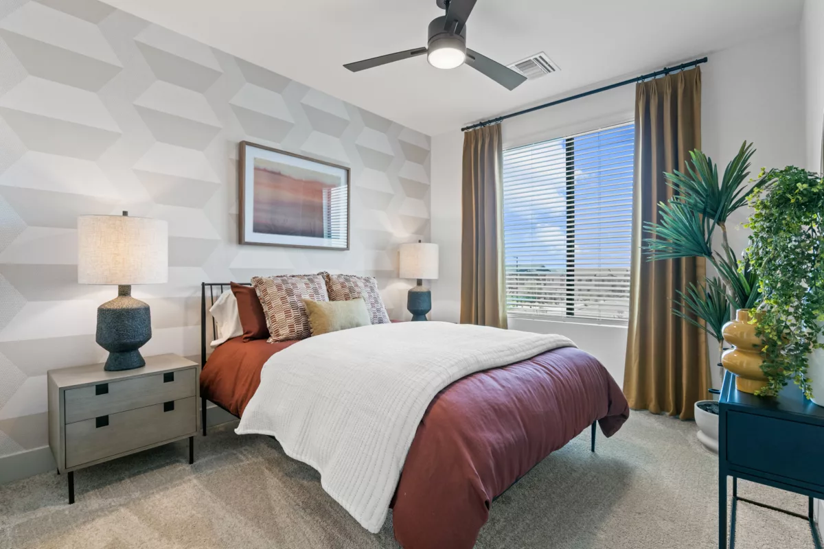 Bedroom with geometric wallpaper, bed with rust bedding, and a ceiling fan.