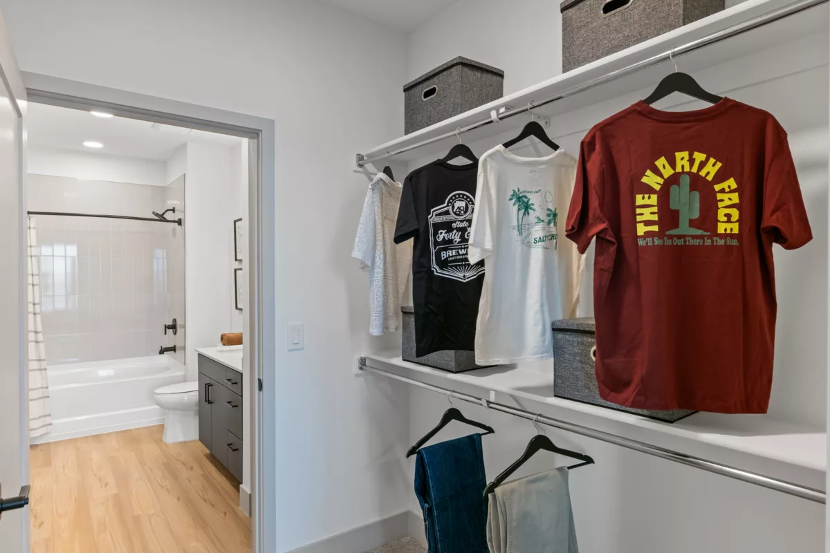 Walk-in closet with shelving, clothing, and storage bins. Bathroom visible in background.