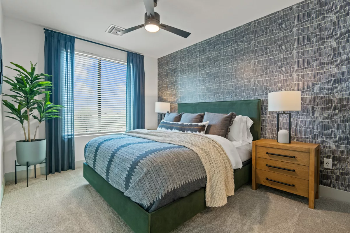 Bedroom with green bed frame, blue wallpaper, and wood nightstand with lamp.