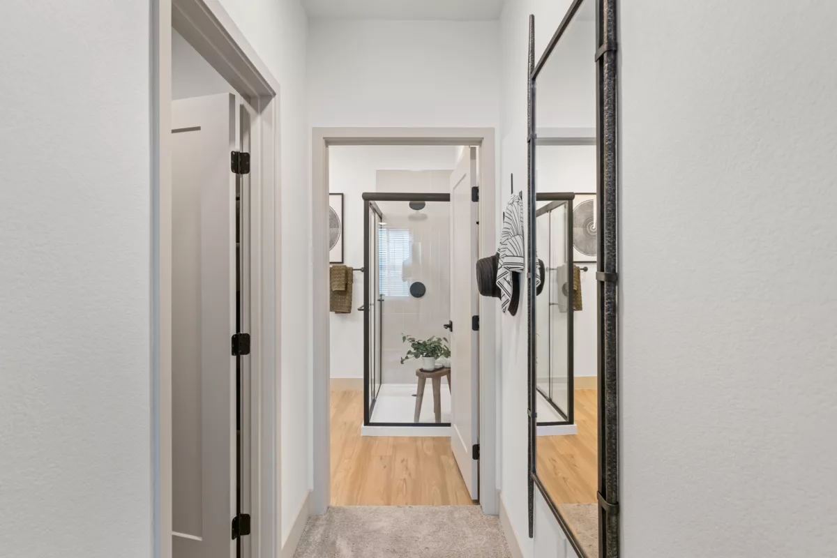 Hallway view into bathroom with glass shower, wood floors, and decorative mirror.