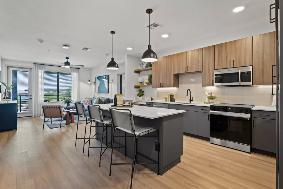 Open-concept kitchen with island, gray cabinets, wood accents, and stainless steel appliances.