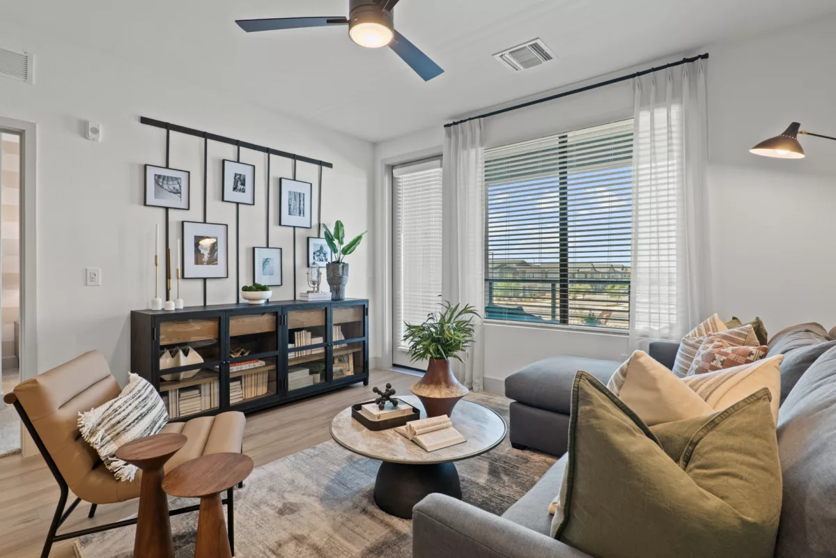 Living room with gray sofa, wood floors, console table, and large window with blinds.