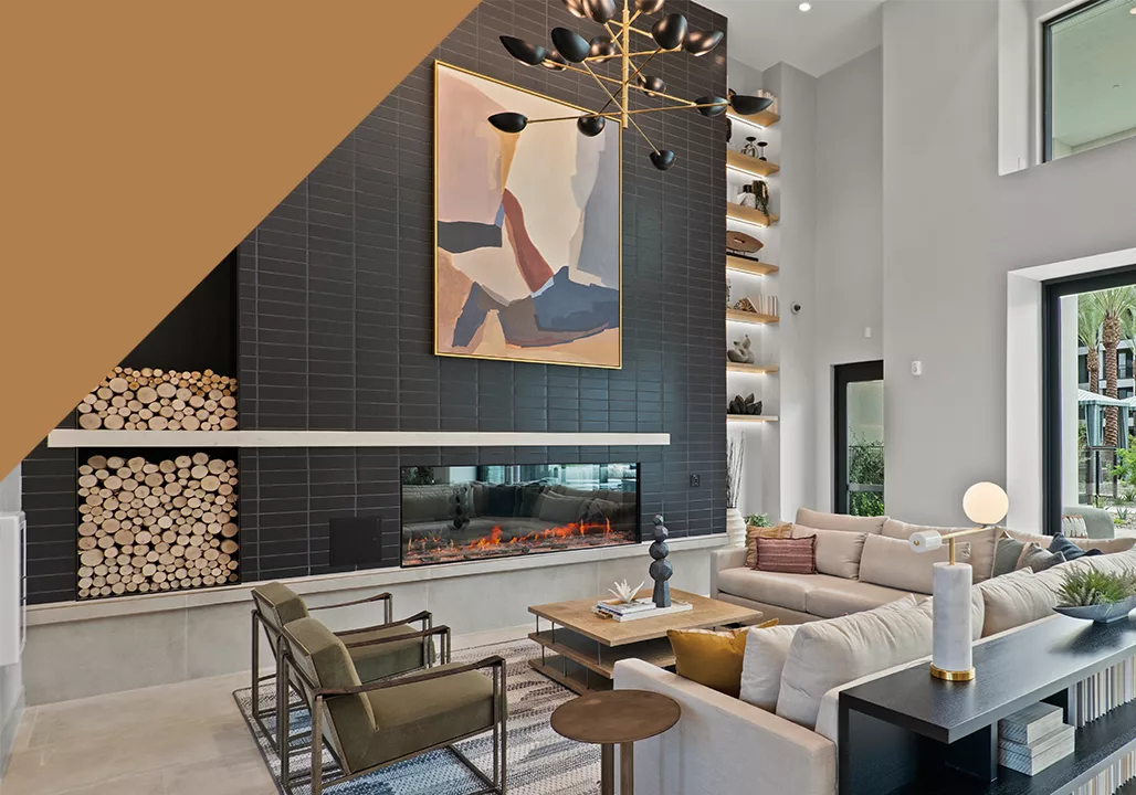 A photo of a lounge with a fireplace, chairs, couches, and a modern chandelier, with a decorative orange triangle in the upper left corner.
