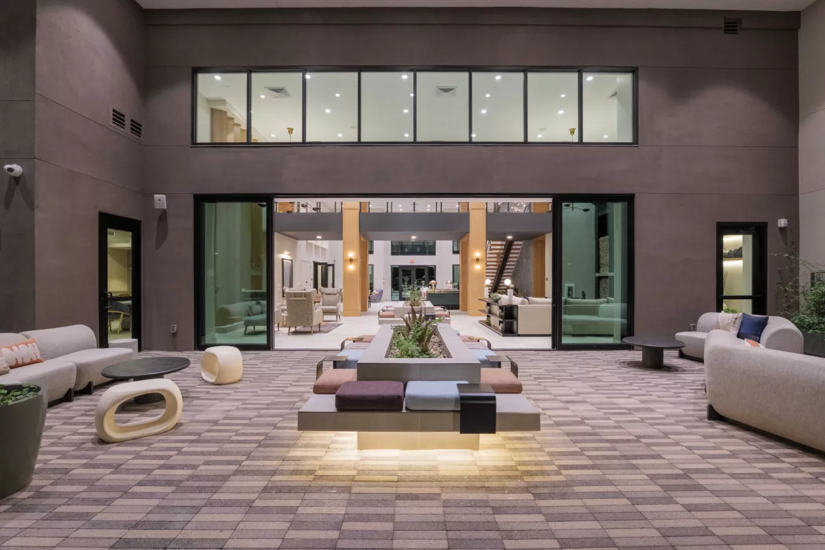 Indoor lounge area features modern seating, a central planter, and a view into another lounge space.