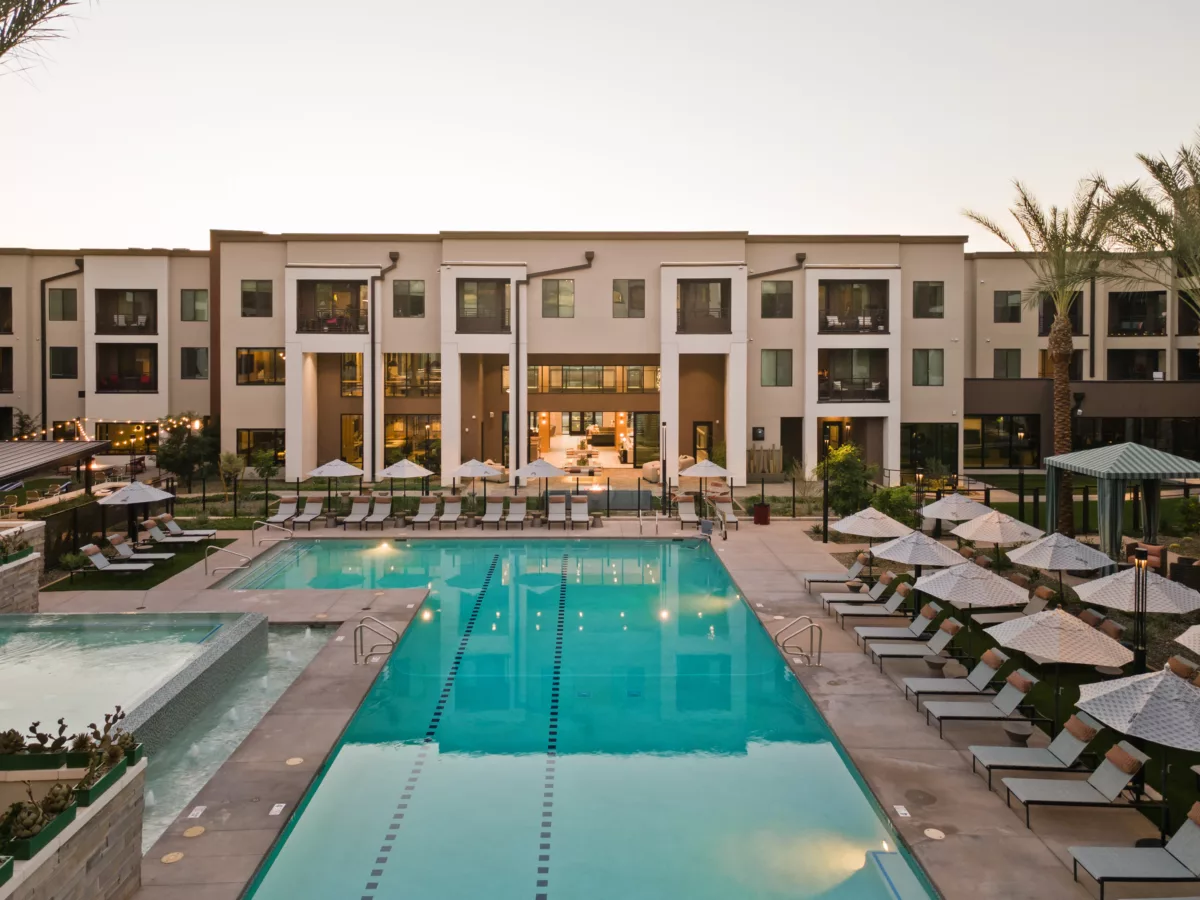 Outdoor pool area with lounge chairs, umbrellas, and a multi-story building in the background.