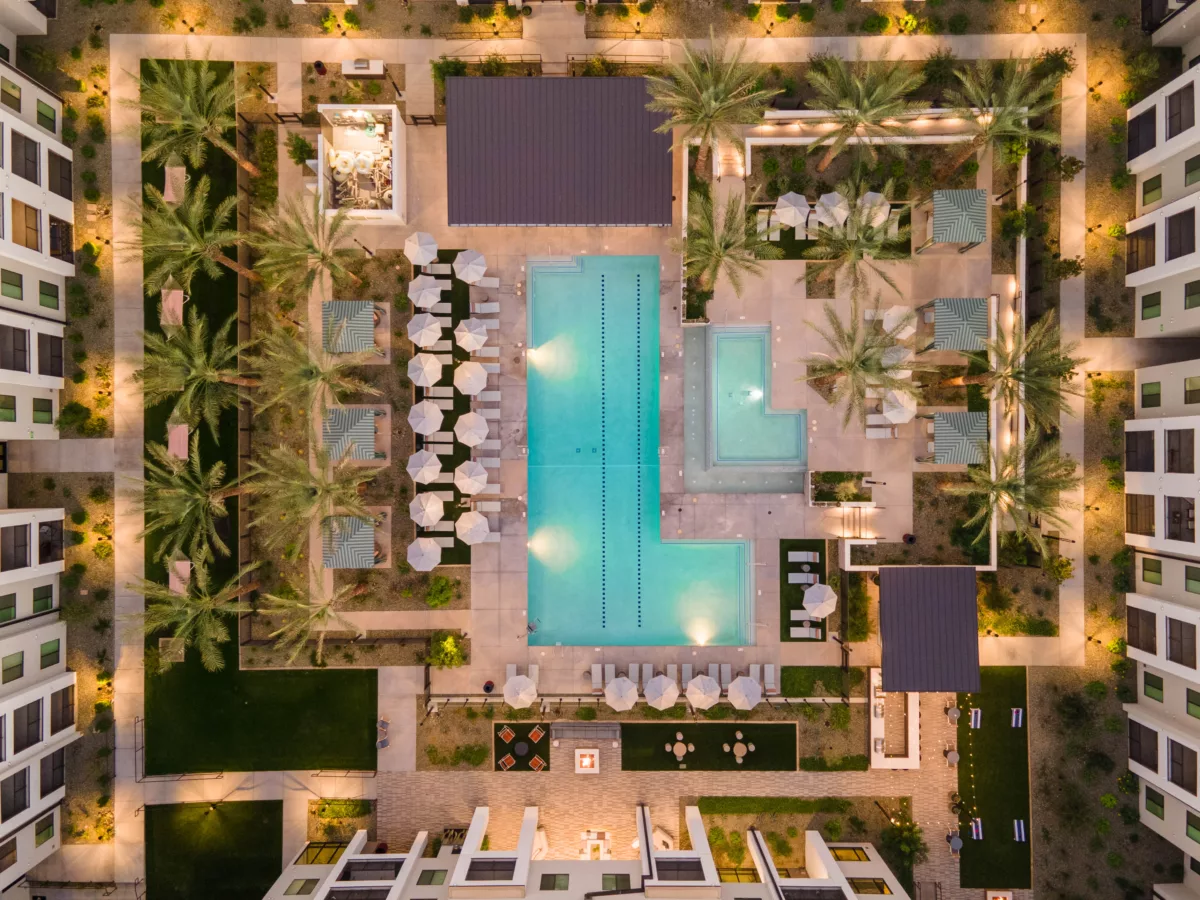 Aerial view of a pool, lounge chairs with umbrellas, and palm trees at dusk.