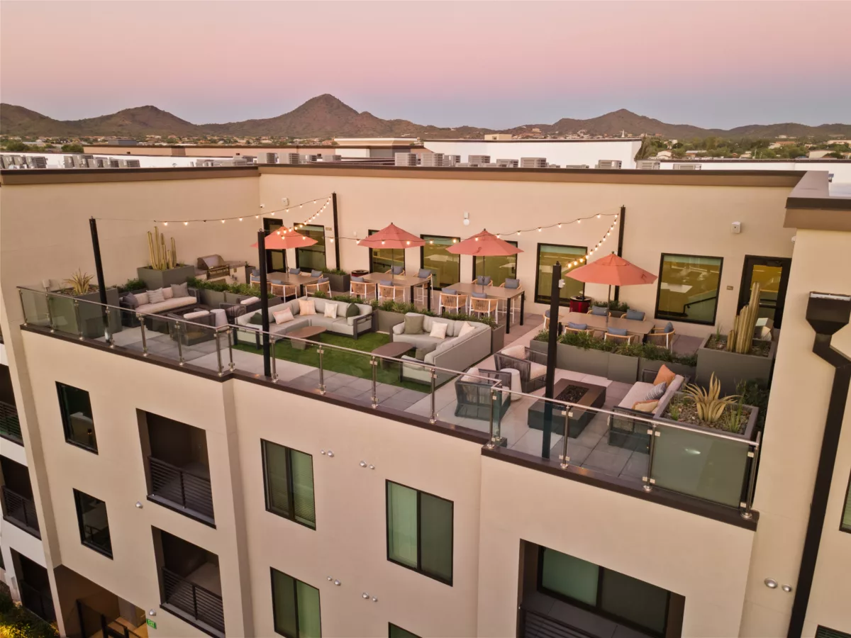 Rooftop amenity space features lounge seating, dining tables with umbrellas, a grill, and mountain views.