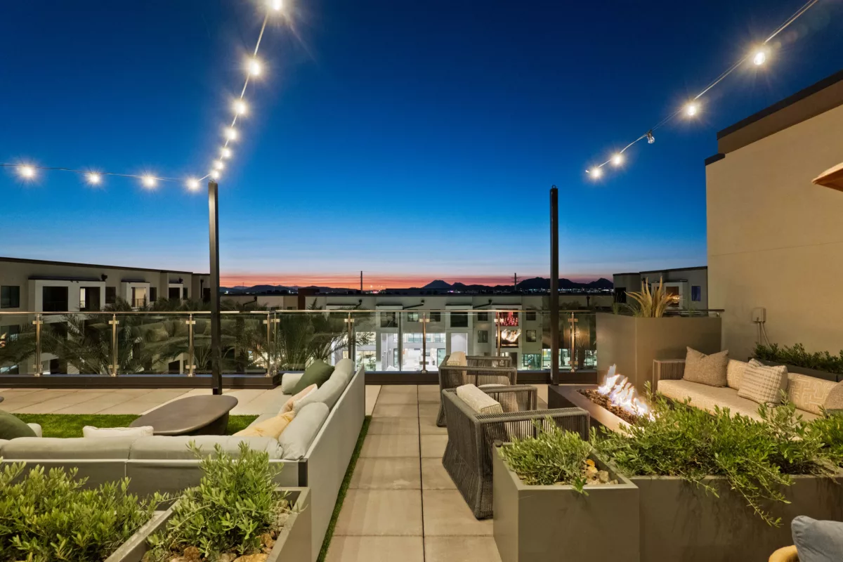 Rooftop lounge area features outdoor seating, a fire pit, string lights, and mountain views at dusk.