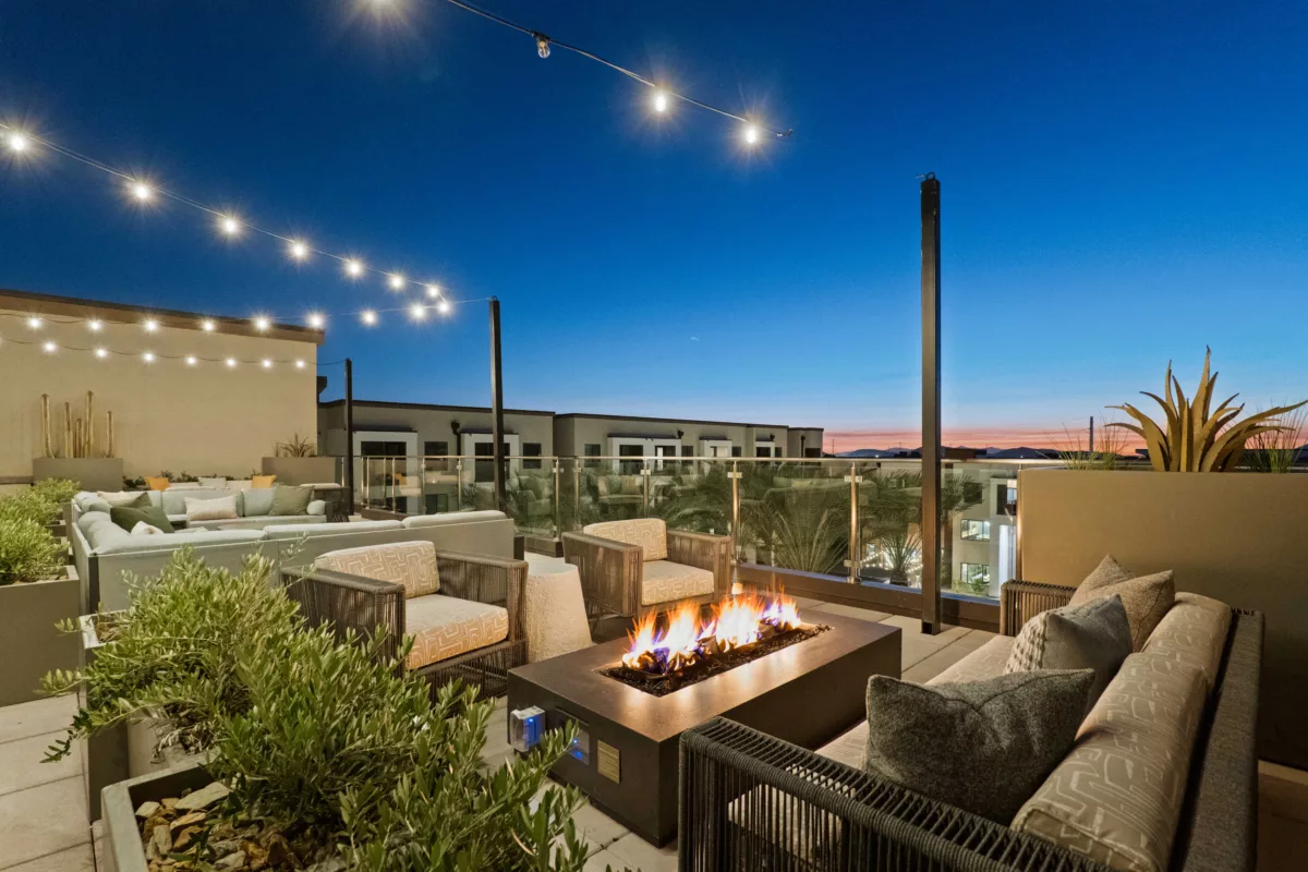 Rooftop lounge features a fire pit, seating, string lights, and planters with greenery.