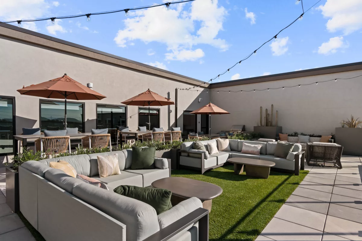 Outdoor lounge area with patio furniture, dining tables with umbrellas, and string lights.