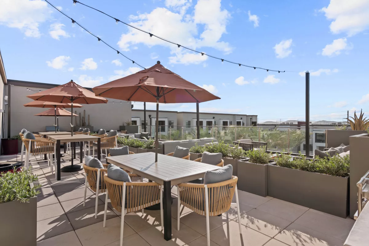 Outdoor lounge area with tables, chairs, umbrellas, and planters on a rooftop patio.