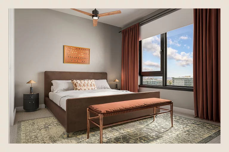 Bedroom with brown bed, ceiling fan, and large window with city view