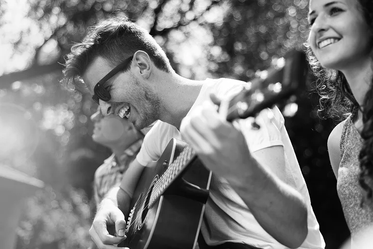 People smiling outdoors as a man plays acoustic guitar