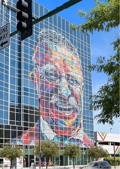 Colorful mural of a man’s face on glass building in downtown setting