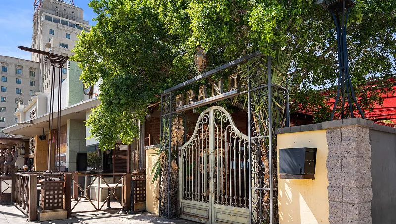 Ornate metal gate labeled “GRAND” with trees and buildings behind