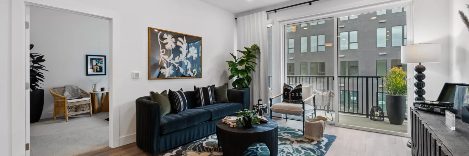 Modern living room with dark sofa, floral rug, and sliding glass door to balcony.