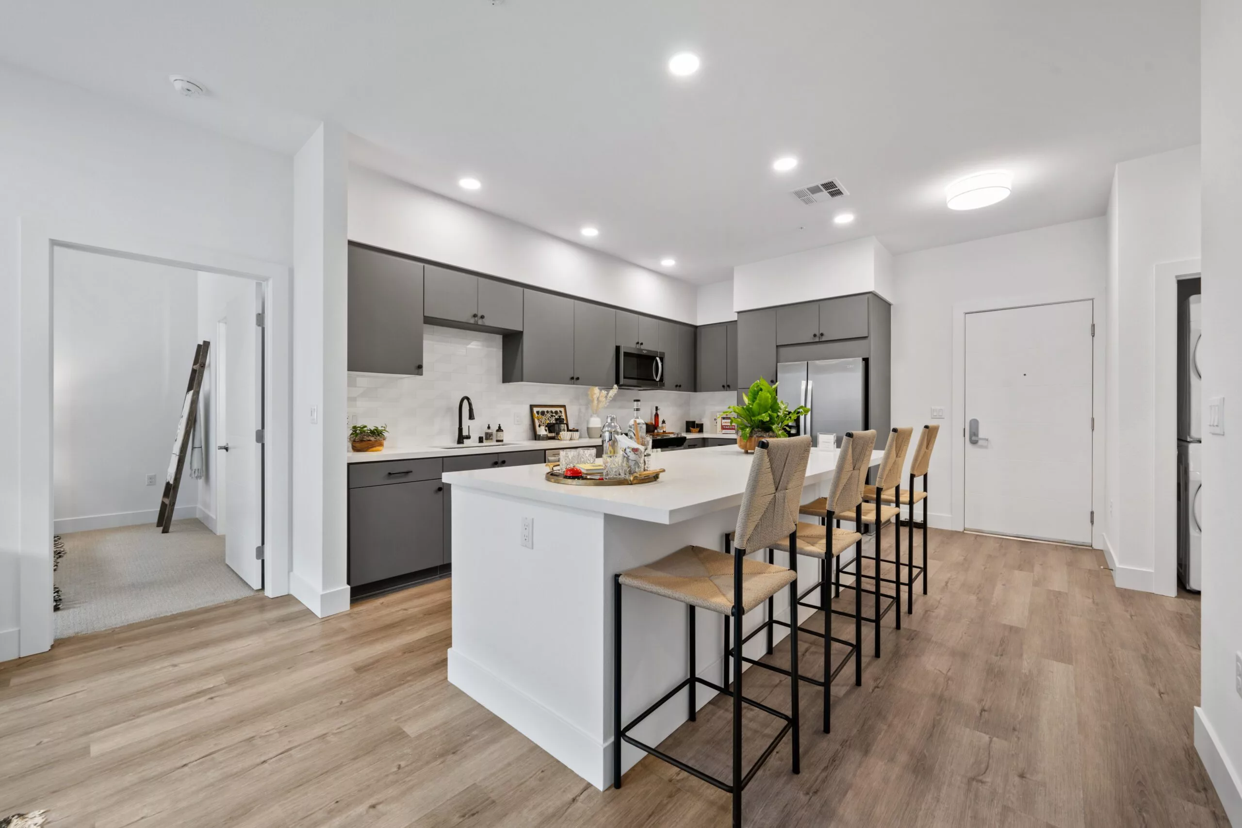 Modern kitchen with gray cabinets, white island, and four barstools on wood flooring.