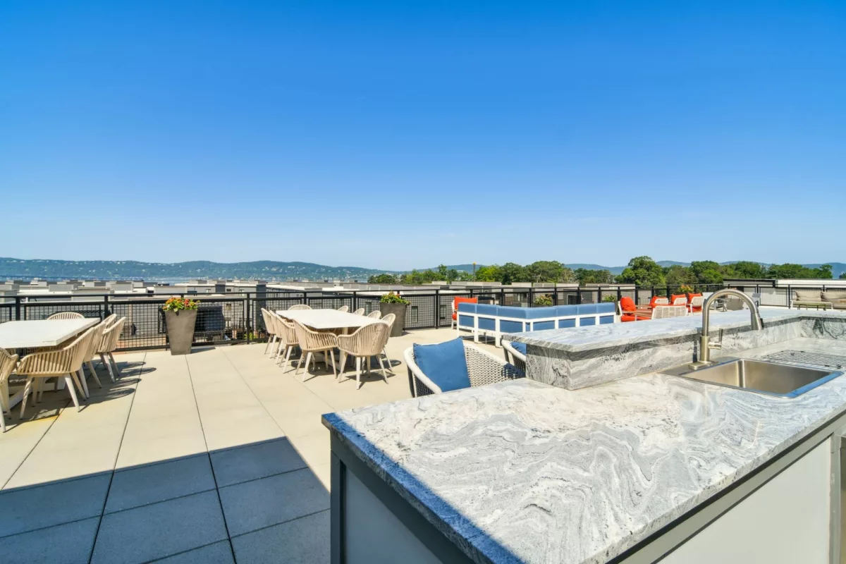 Outdoor rooftop kitchen and lounge seating with a view of green trees and a river in the background.