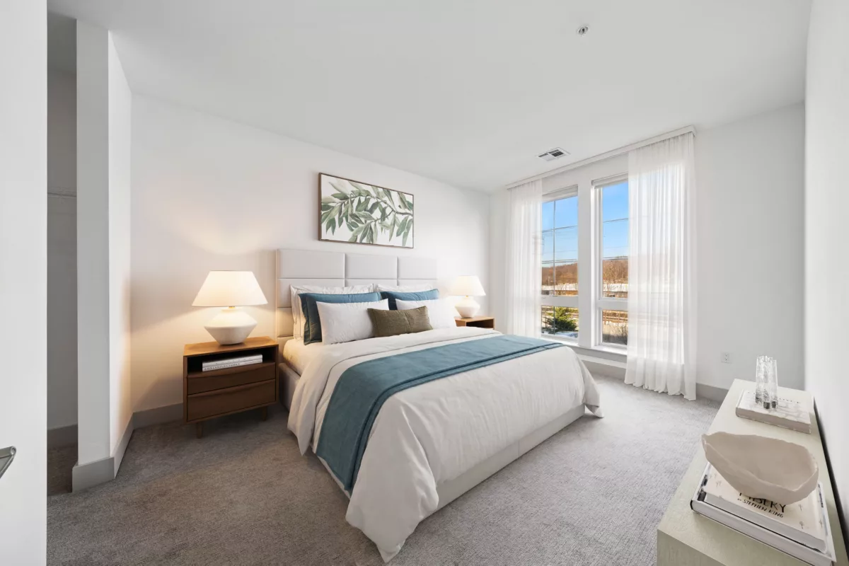 A modern bedroom with a queen-sized bed, two nightstands, and a large window with sheer curtains.