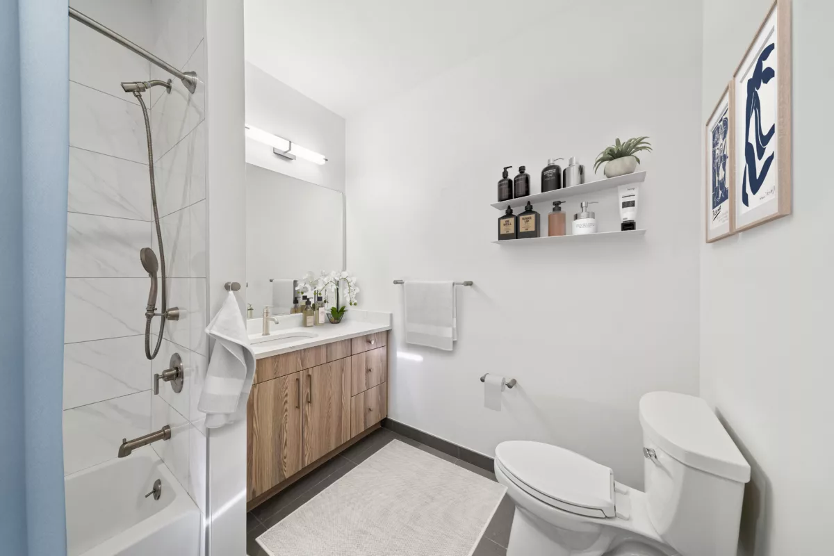 Modern bathroom with a wood vanity, white countertop, and a shower-tub combination with white tile.
