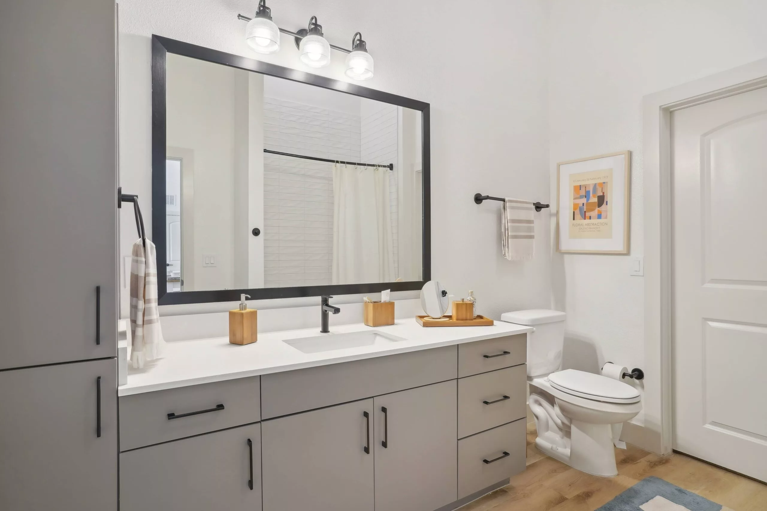 Modern bathroom with large mirror, gray vanity, and wood-accented accessories.