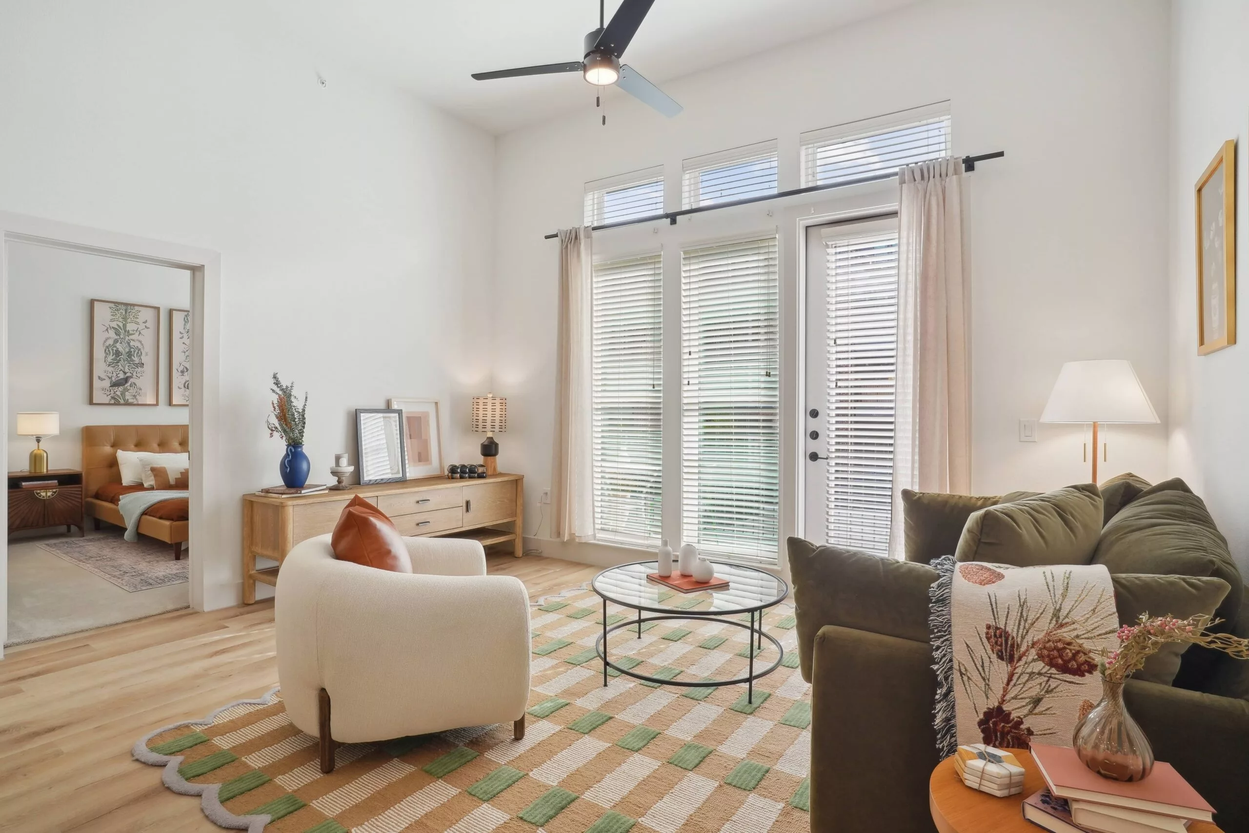 Bright living room with green sofa, checkered rug, and tall windows with blinds.