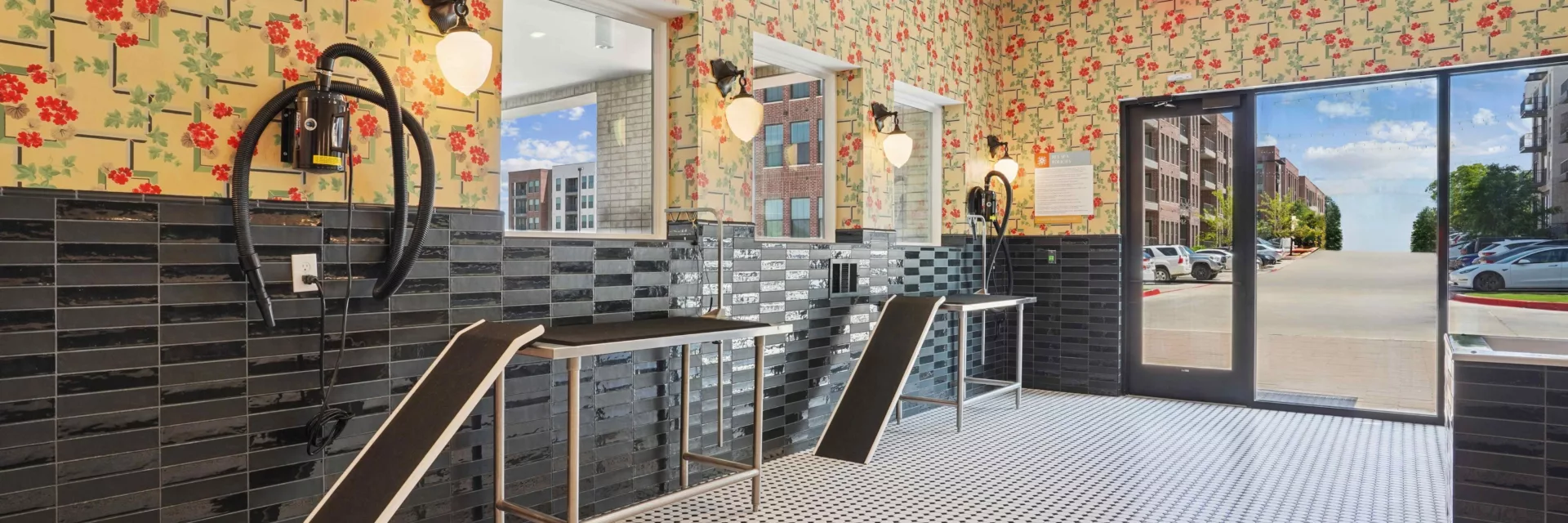 Colorful pet wash station with floral wallpaper, black tile, and grooming tables with ramps.