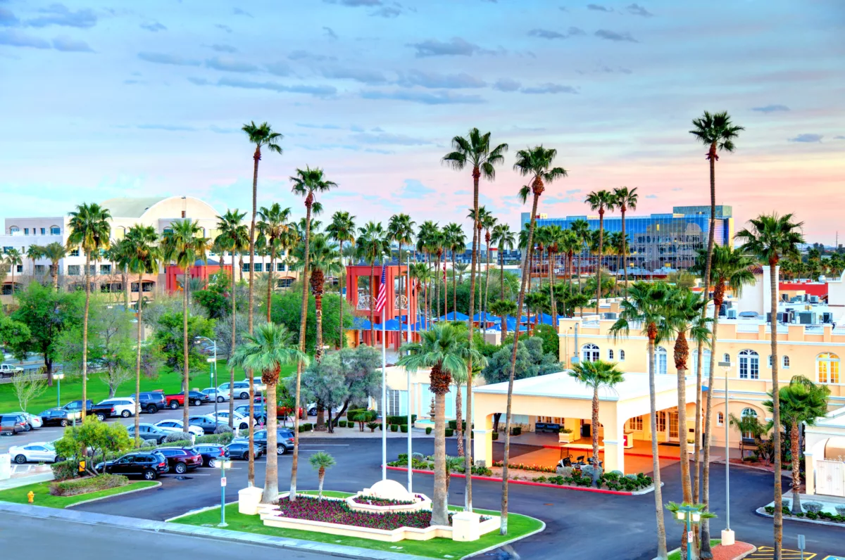 Urban scene with palm trees, yellow building, cars, and pastel sunset sky.