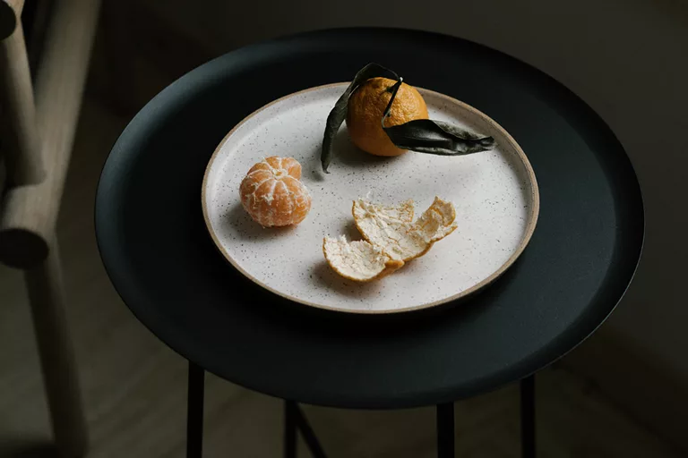 Plate with peeled and whole tangerines on dark round table.