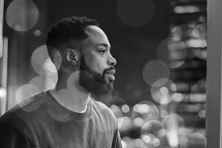 Man looking out window at night with blurred city lights.